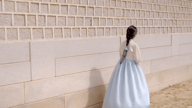 Woman in hanbok walking along a stone wall