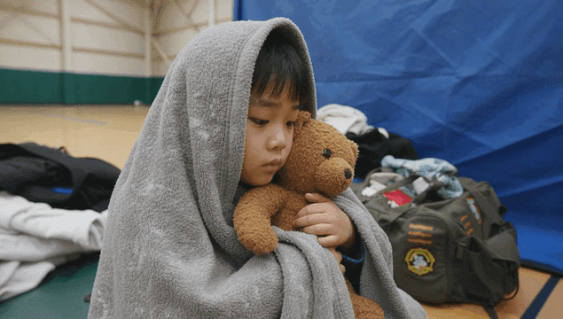 체육관 대피소에서 담요에 싸여 곰인형을 안고 있는 아이