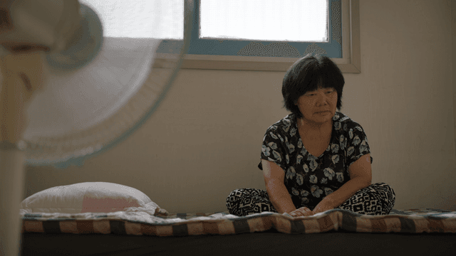 An elderly woman sitting on a bed indoors
