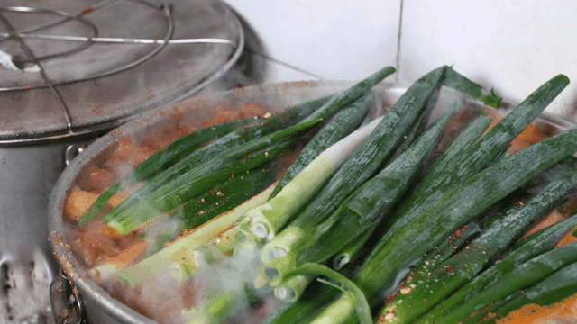 Chef adding green onions to pot of boiling spicy broth