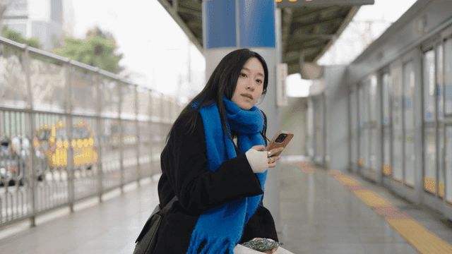 Woman waiting for a train at a subway station with her smartphone in her hand