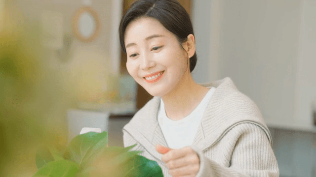 미소를 지으며 실내 식물을 돌보는 여성