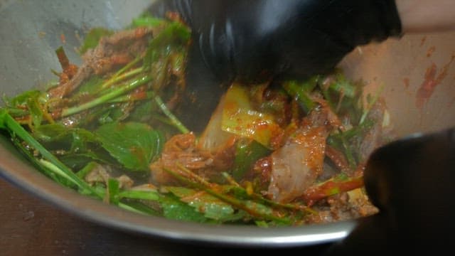 Mixing steamed meat and vegetables with seasoning in a metal bowl