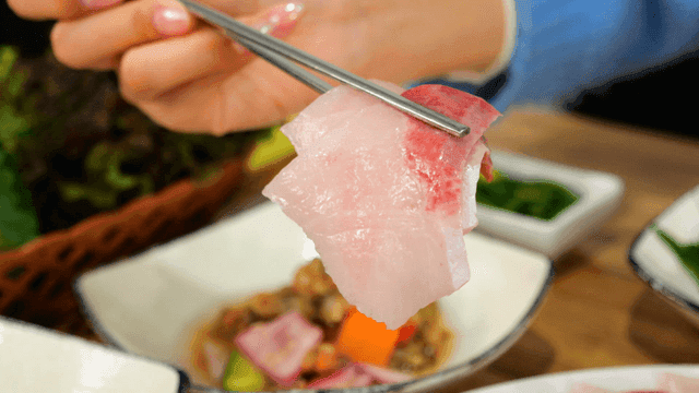 Fresh yellowtail sashimi picked up with chopsticks