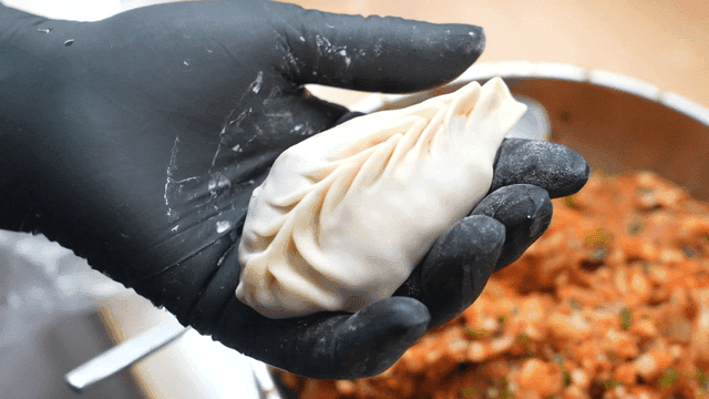 Gloves holding filled kimchi dumpling