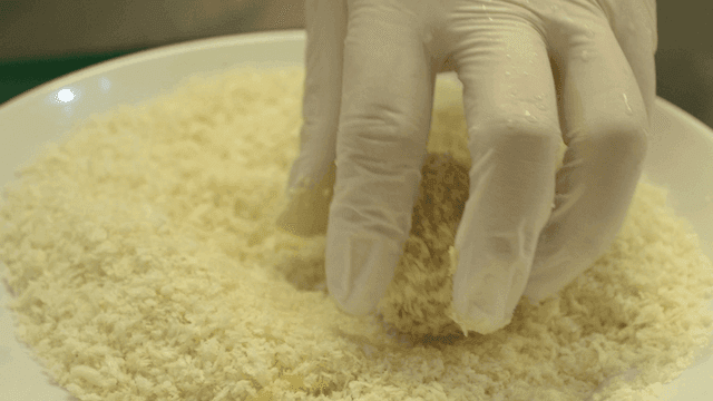 Hands dipping fried dough in breadcrumbs