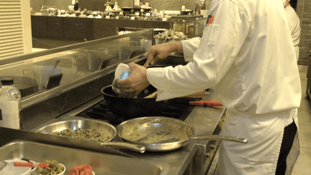 Chef pouring ingredients into pan in busy kitchen