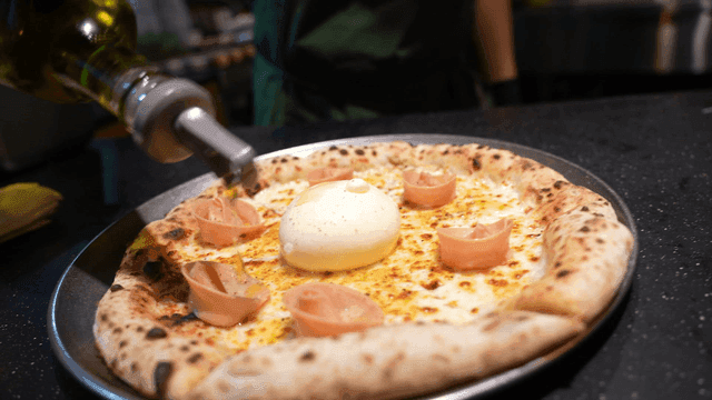 Olive oil drizzled over Mortadella Burrata pizza topped with burrata cheese and ham