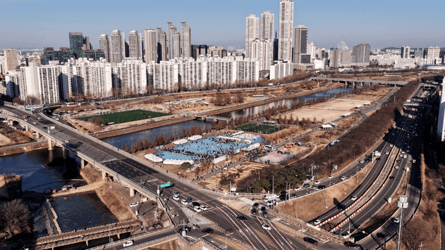 People gathered at riverside sports field in bustling city with high-rise buildings