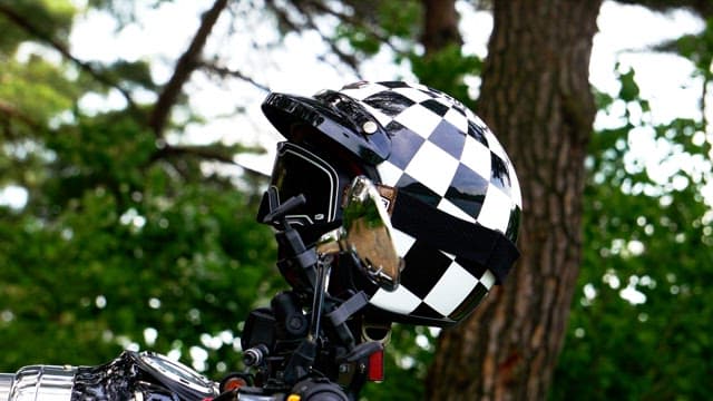 Motorbike helmet with checkered pattern against a forest backdrop.