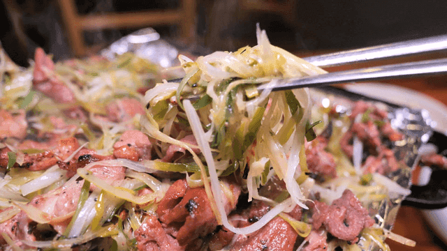 Chopsticks picking up charcoal-grilled green onion bulgogi on hot iron plate