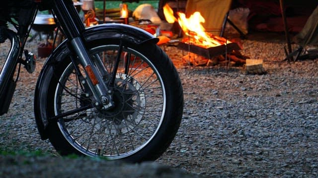 Motorcycle parked beside a campfire in a gravel lot at dusk