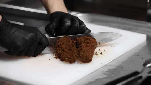 Hands slicing black pork cutlets on cutting board