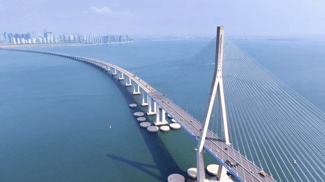 A long bridge over a vast sea with a city skyline