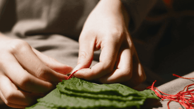 Hands tying perilla leaves with red thread