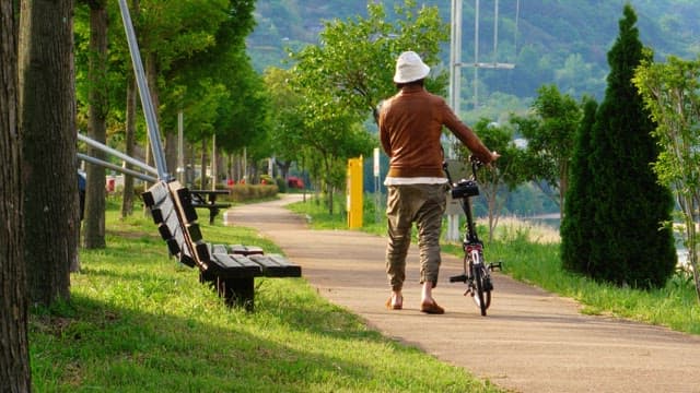 Man walking his bike on a park pathway