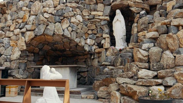 Statue of woman praying with a stone sculpture of Virgin Mary in a rocky outdoor shrine