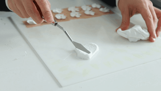 Hands shaping white clay with craft spatula