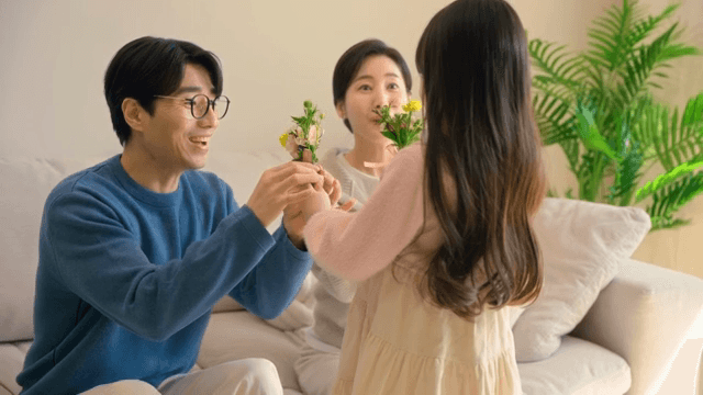 소파에 앉아있는 부모님께 카네이션을 선물하는 아이