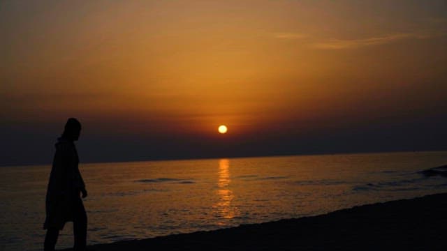 일몰의 붉은 하늘 아래 홀로 바닷가를 걷는 사람