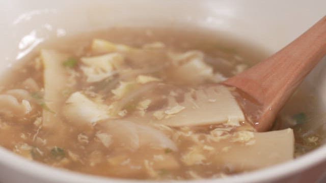 Wooden spoon stirring warm soup with bamboo shoots