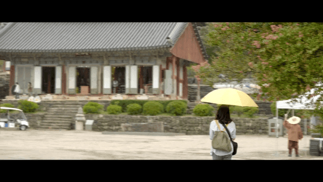 Woman holding yellow umbrella walking toward traditional Korean temple