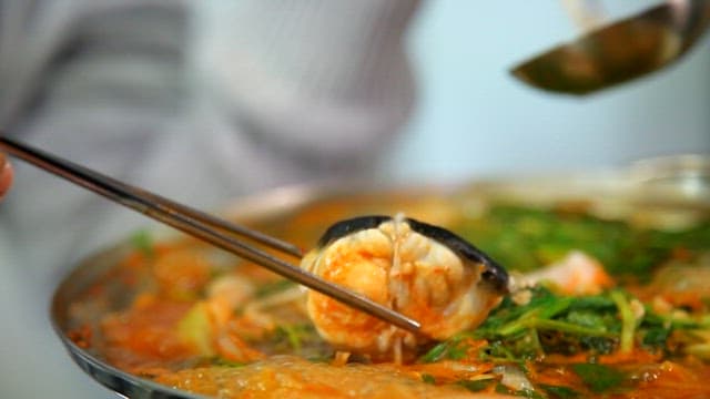 Ladleful of kimchi stew with puffer fish, vegetables and seafood