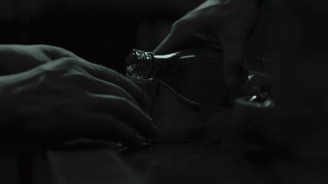 Person pouring soju into glass on dark table