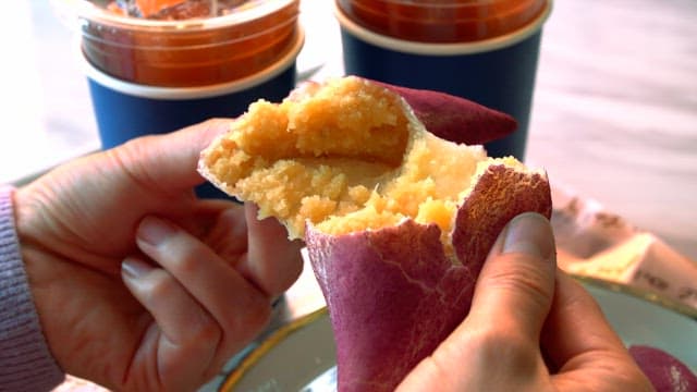 Hands breaking sweet potato bread against background of iced coffee cup