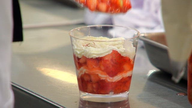 Preparing dessert by placing strawberry slices in a glass with cream