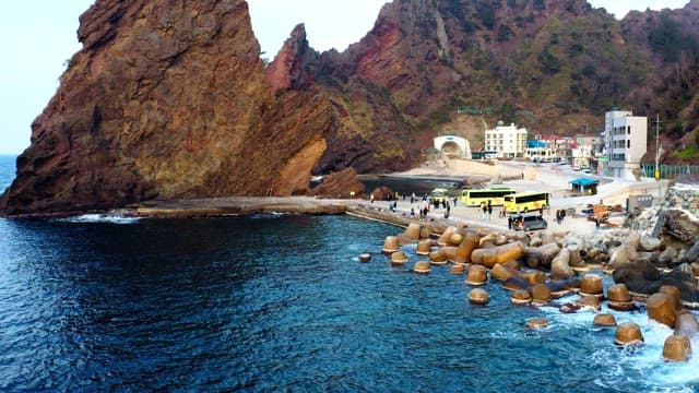 Coastal town by a rocky sea cliff with parked buses and people