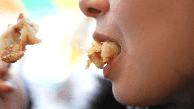 Mouth of woman eating hot potato pancake with relish