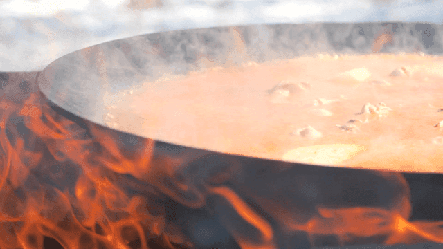 Chicken stew cooked on large pot lid over fire