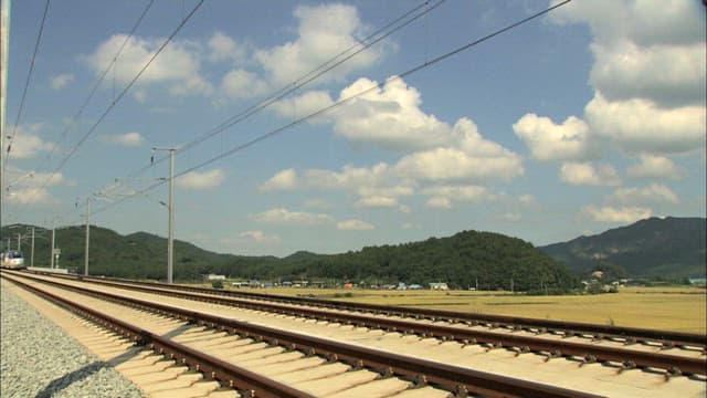 High-speed train passing through countryside, surrounded by hills and fields under a bright sky