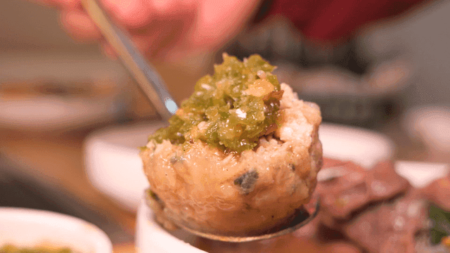Spoon containing rolled dumplings topped with chopped chili peppers