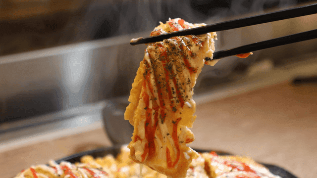 Chopsticks holding omelet topped with sauce on hot iron plate