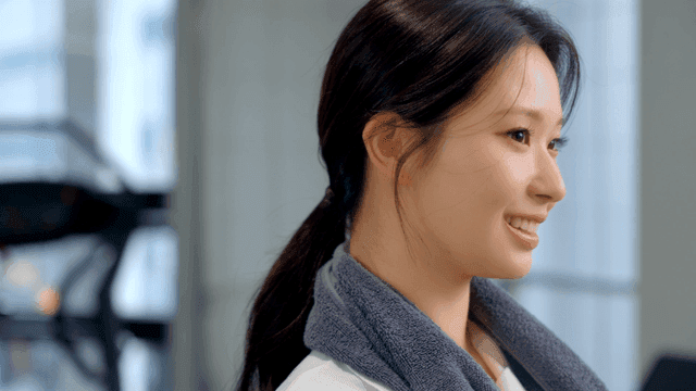 헬스장에서 수건을 목에 매고 미소짓는 여성의 옆모습