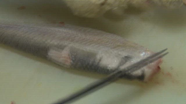 Sliced raw scaled sardine being prepared on a cutting board in a sushi restaurant kitchen