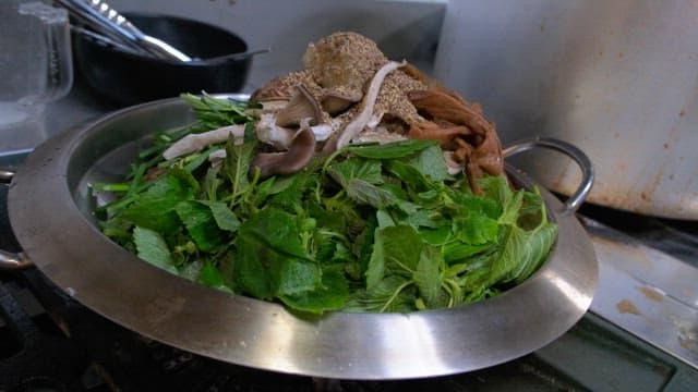 Fresh greens and mushrooms in a metal bowl for hotpot dish