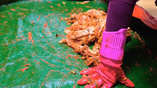 Kimchi being mixed with spices on a mat