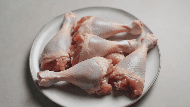 Raw chicken drumsticks on a white plate