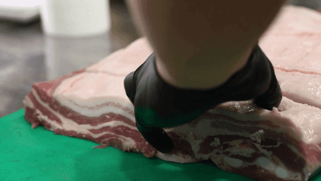 Hands cutting pork belly on cutting board