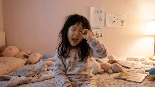 Child waking up in cozy bedroom and rubbing their eyes