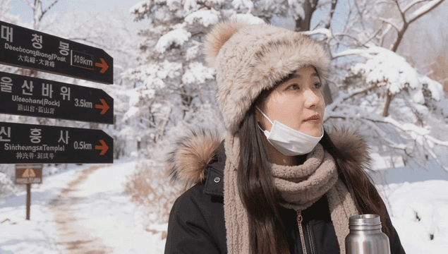 눈 덮인 산길 이정표 옆에서 보온병을 마시는 여성
