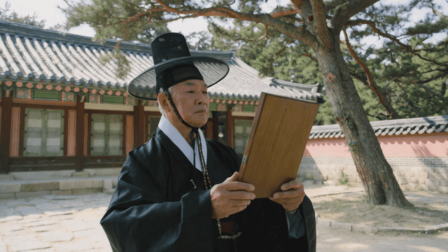 Scholar in traditional Hanbok reading woodblock