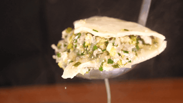 Ladle scooping out boiling dumpling soup from pot