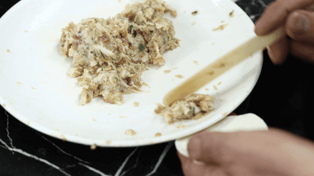 Hands putting dumpling filling from white plate into dumpling wrappers