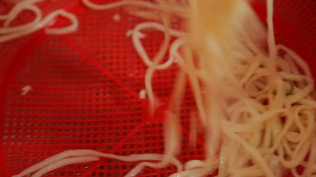 Noodle soup being rinsed in a red strainer