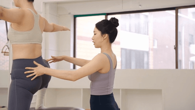 Pilates instructor assists a student indoors