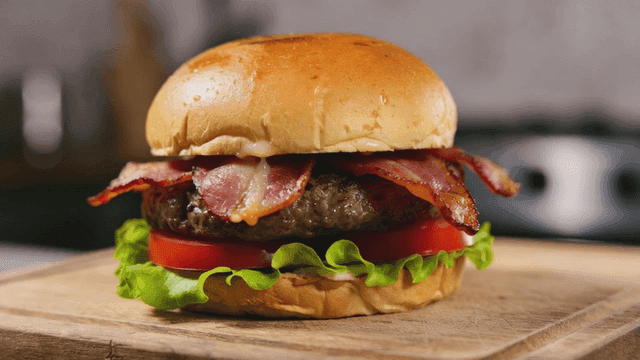 Delicious bacon cheeseburger on cutting board.